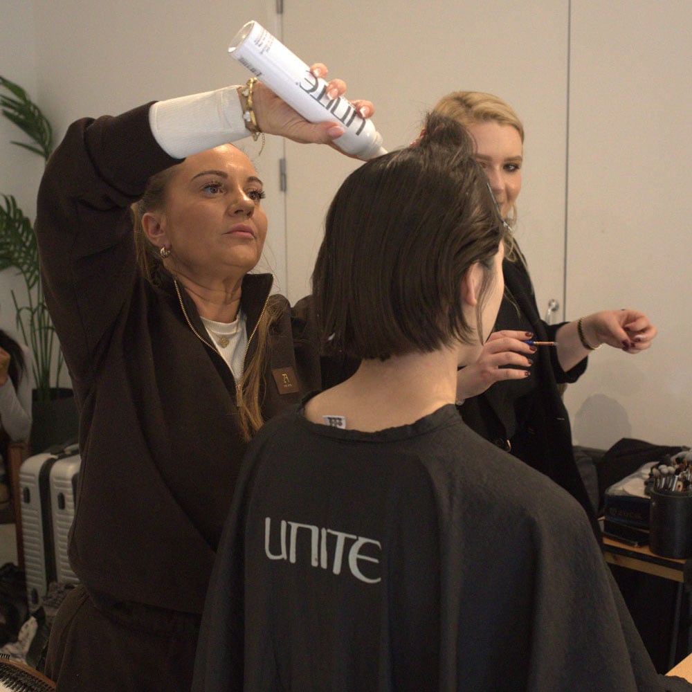 Hairstylist backstage die een korte bob stylet voor een catwalklook.